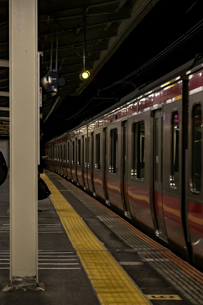 A Tokyo metro train waiting at a dimly lit platform at night, capturing the ambiance of urban commute.